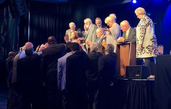 Newly elected Bishops kneel as the previous Board of Bishops and Board of Administrators lays hands on them. 